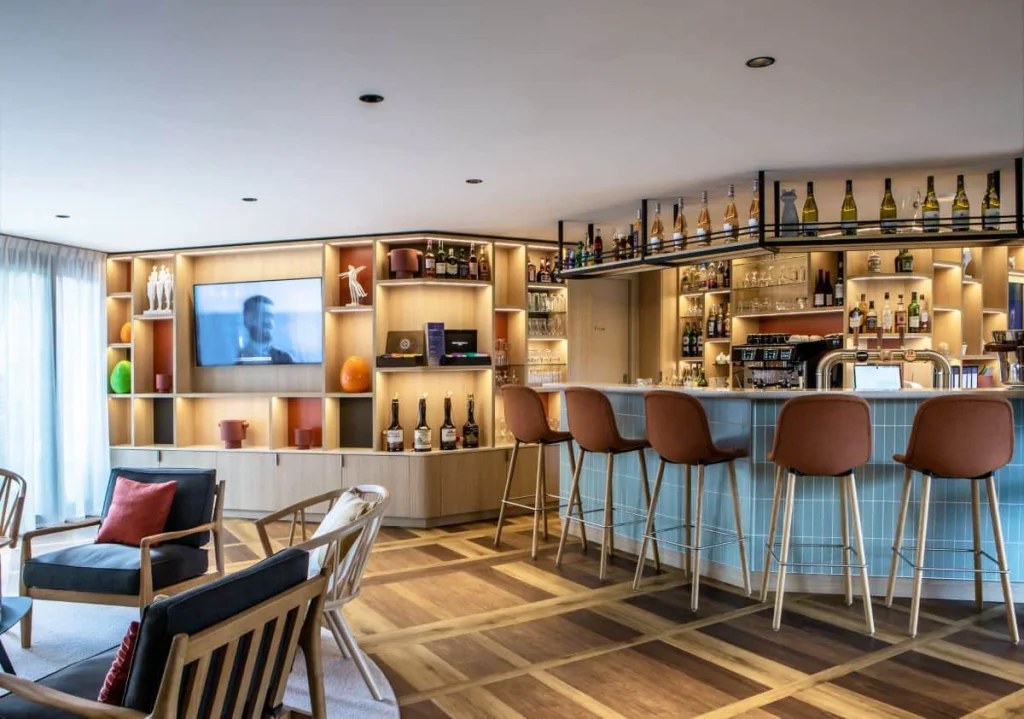 Bar et lounge de l’Hôtel Antares & Spa Honfleur avec comptoir éclairé, chaises hautes et espace détente confortable.