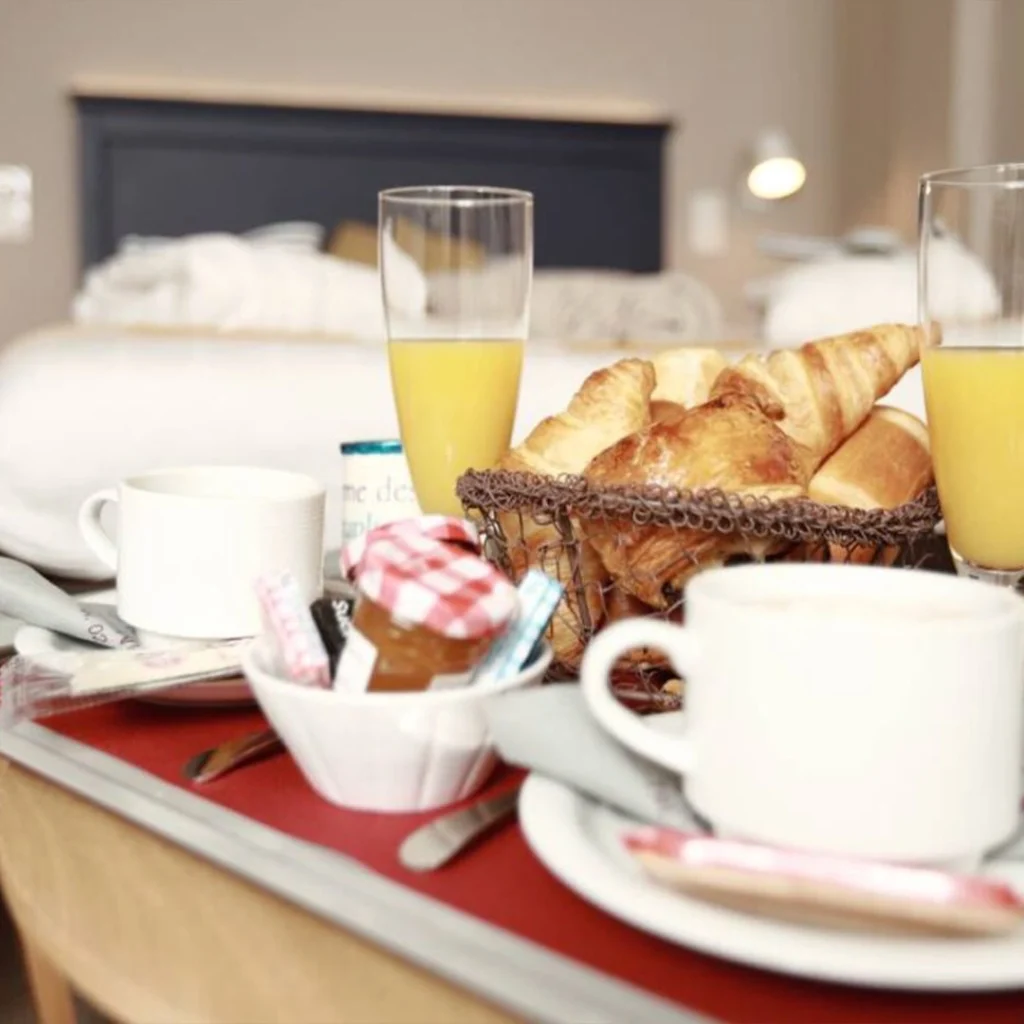 Beeld van het aanbod “De Grote Ontsnapping: 1 nacht” van Hôtel Antares & Spa Honfleur, met een warme ontbijtscène met viennoiseries en drankjes.