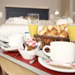 Beeld van het aanbod “De Grote Ontsnapping: 1 nacht” van Hôtel Antares & Spa Honfleur, met een warme ontbijtscène met viennoiseries en drankjes.