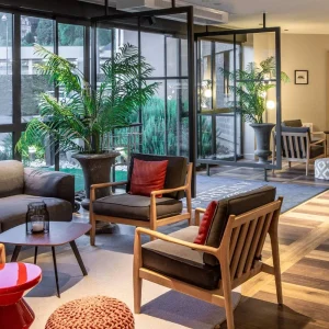 Salon avec verrière de l'Hôtel Antarès Honfleur, fauteuils en bois et plantes vertes en Normandie