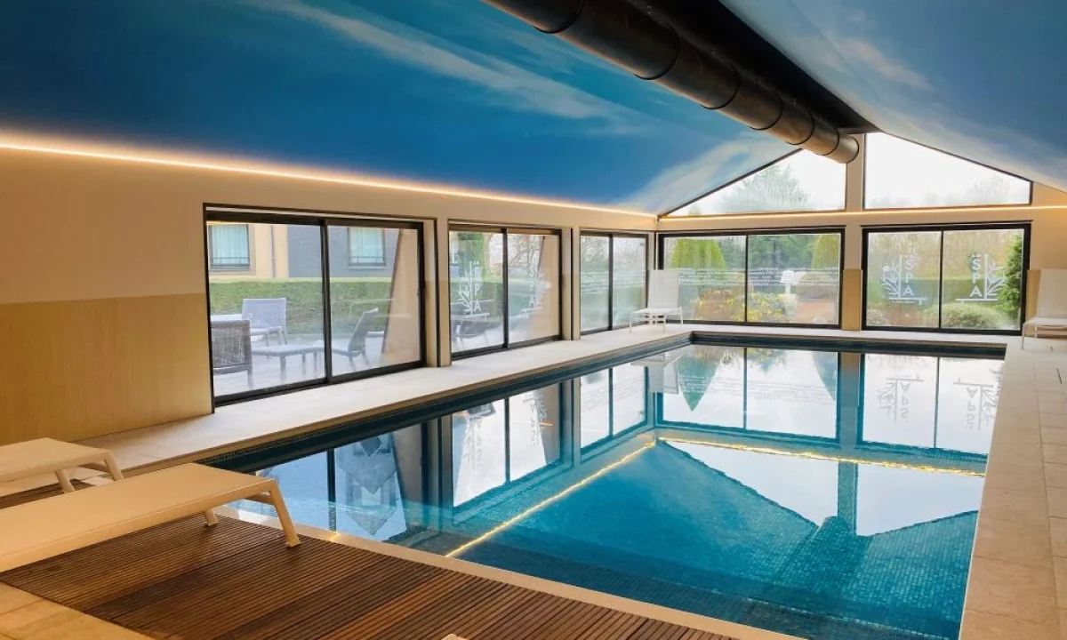 Indoor pool with lounge chairs, large picture windows and blue ceiling at Hôtel Antares & Spa Honfleur.